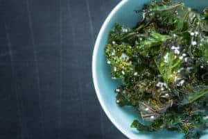Kale chips with salt in pastel blue bowl captured from above (top view). Healthy dietetic snack. Black chalkboard as background. Background layout. Healthy Snacks for When You Get the Munchies. Kale Looks Like Marijuana.